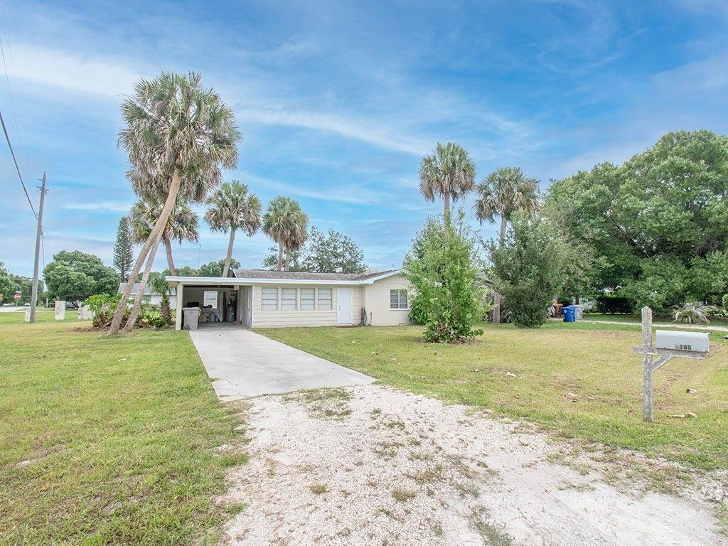 A single-story house with light siding, a carport, and a gravel driveway under a blue sky — VERO BEACH, FL