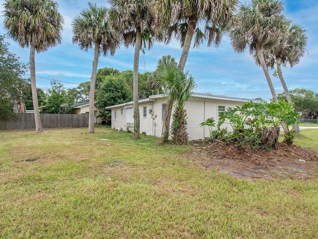 A side view of a single-story house with a grassy yard and several palm trees — VERO BEACH, FL