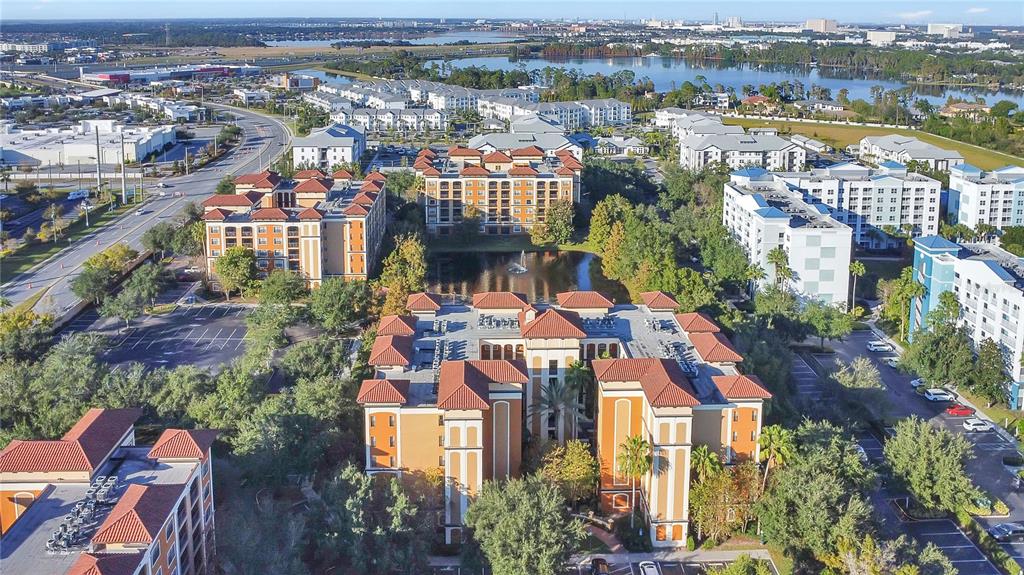 An aerial view shows several multi-story apartment buildings with orange roofs surrounding a small pond — 12539 FLORIDAYS RESORT DRIVE UNIT 203D, ORLANDO, FL