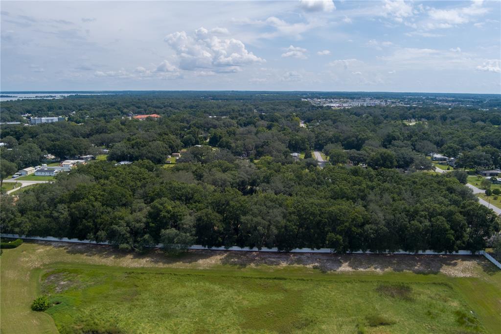 An aerial view shows a large, wooded lot bordered by a white fence and grass — 0 SE 99TH AVENUE, SUMMERFIELD, FL