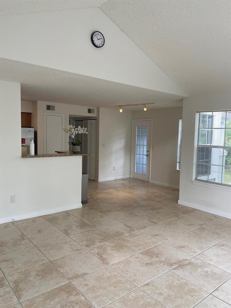 An open-concept living area features vaulted ceilings, beige tile flooring, and a kitchen pass-through window — 1020 Crystal Way # H, Delray Beach FL 33444, DELRAY BEACH, FL