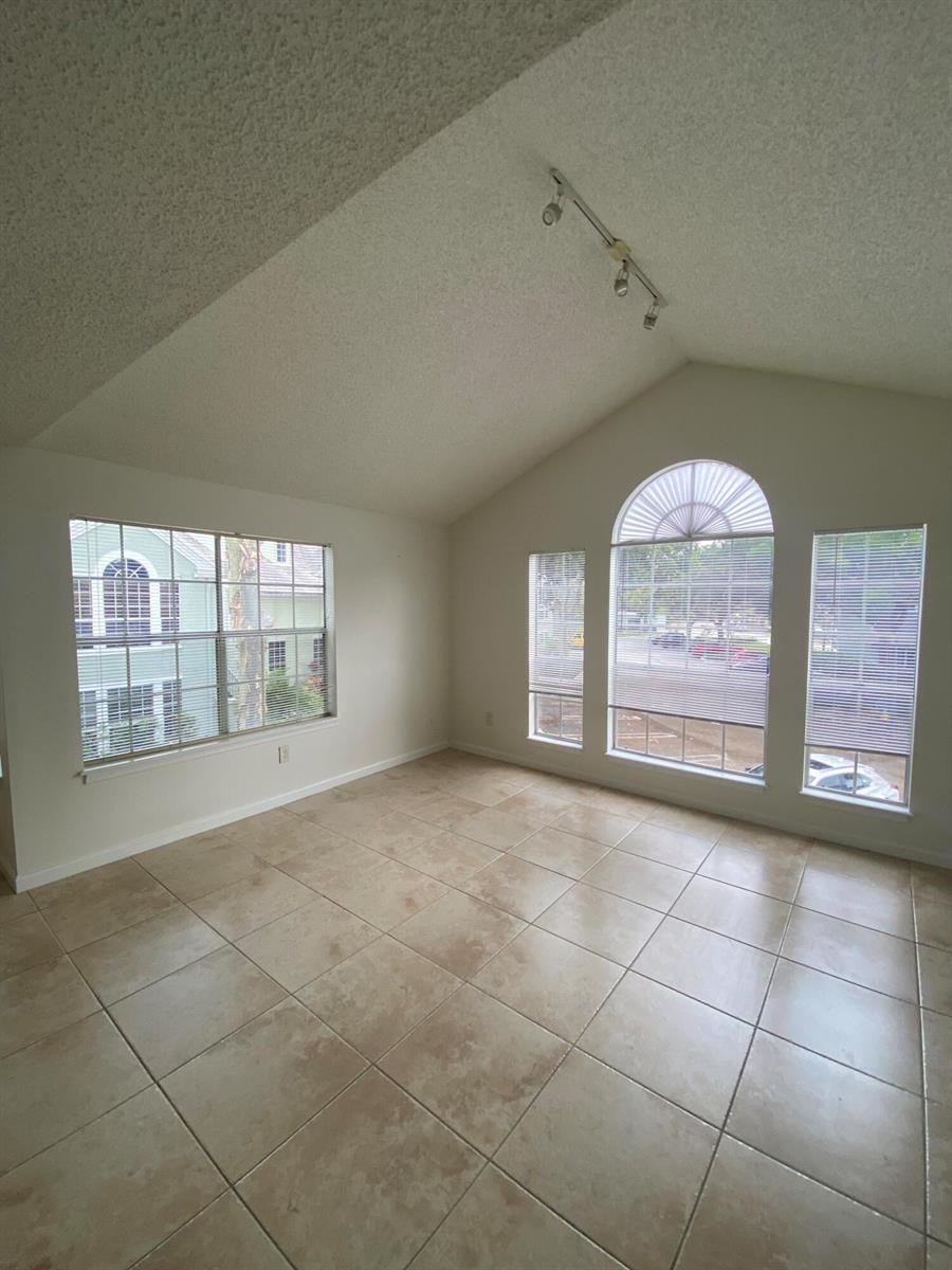 An empty room with vaulted ceilings, tile flooring, and several windows with white blinds — 1020 Crystal Way # H, Delray Beach FL 33444, DELRAY BEACH, FL
