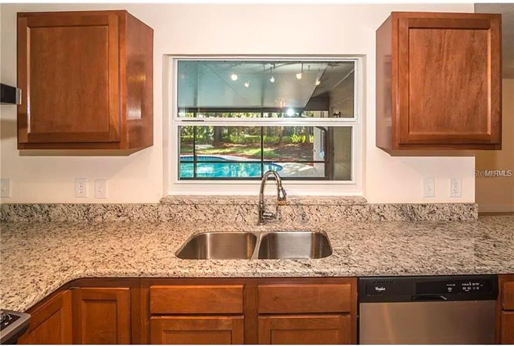 A kitchen sink and granite countertops are positioned beneath a window overlooking a swimming pool — 100 HUNTSWOOD COURT, LONGWOOD, FL