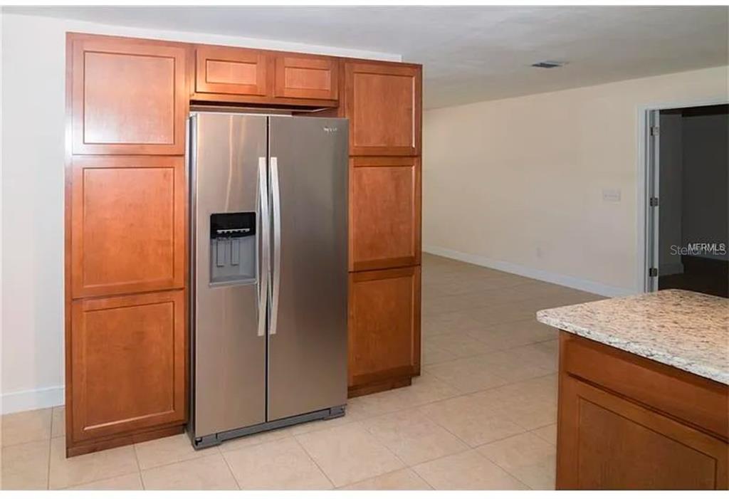 A stainless steel refrigerator is surrounded by wood cabinets in a tiled kitchen area — 100 HUNTSWOOD COURT, LONGWOOD, FL