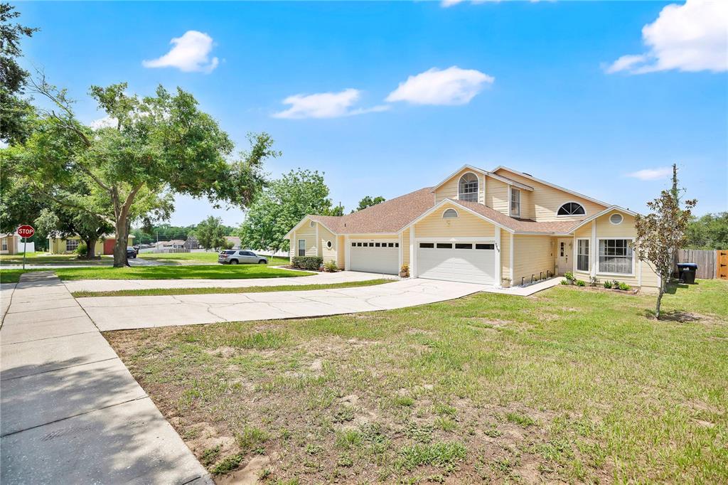 A yellow two-story house with a three-car garage and a large concrete driveway — 7408 LITTLE POND COURT, ORLANDO, FL
