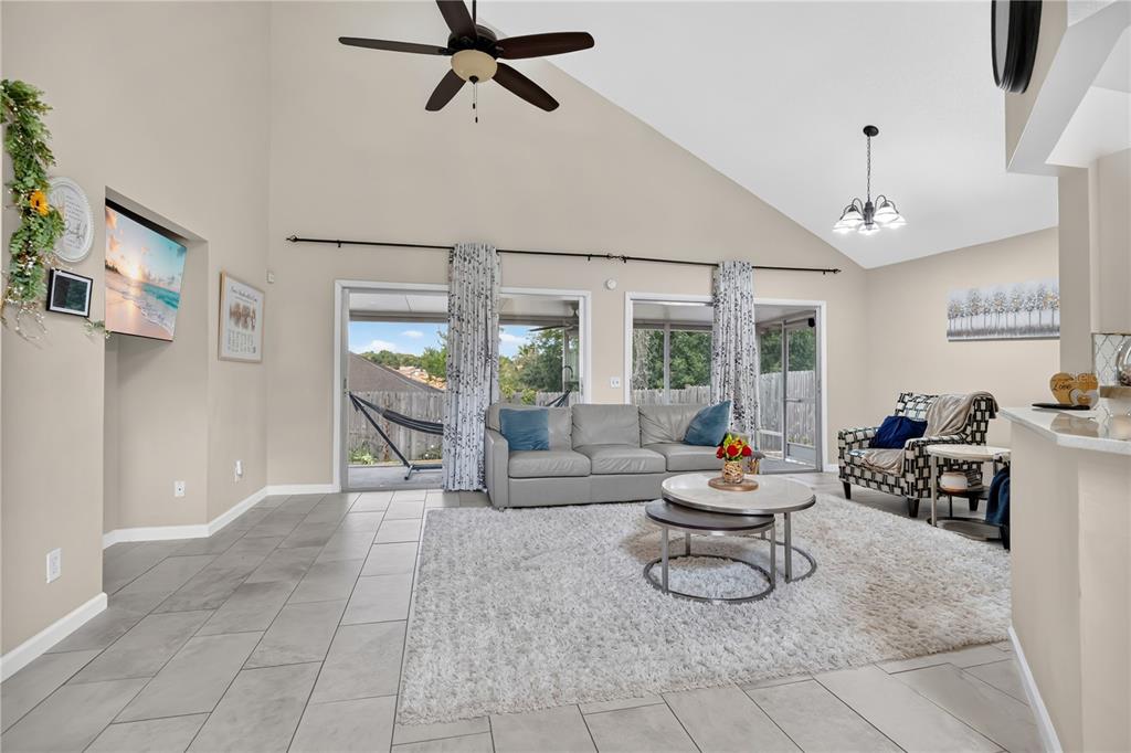 A living room with vaulted ceilings, tile flooring, a gray sofa, and sliding glass doors — 7408 LITTLE POND COURT, ORLANDO, FL