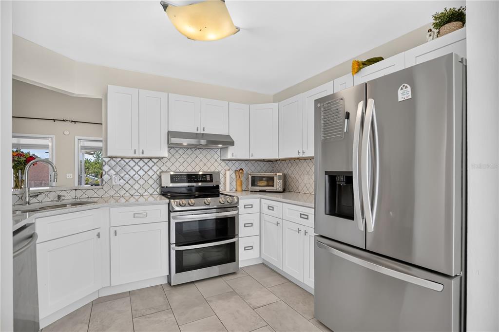 A kitchen features white cabinetry, stainless steel appliances, a tiled backsplash, and light-colored floor tiles — 7408 LITTLE POND COURT, ORLANDO, FL
