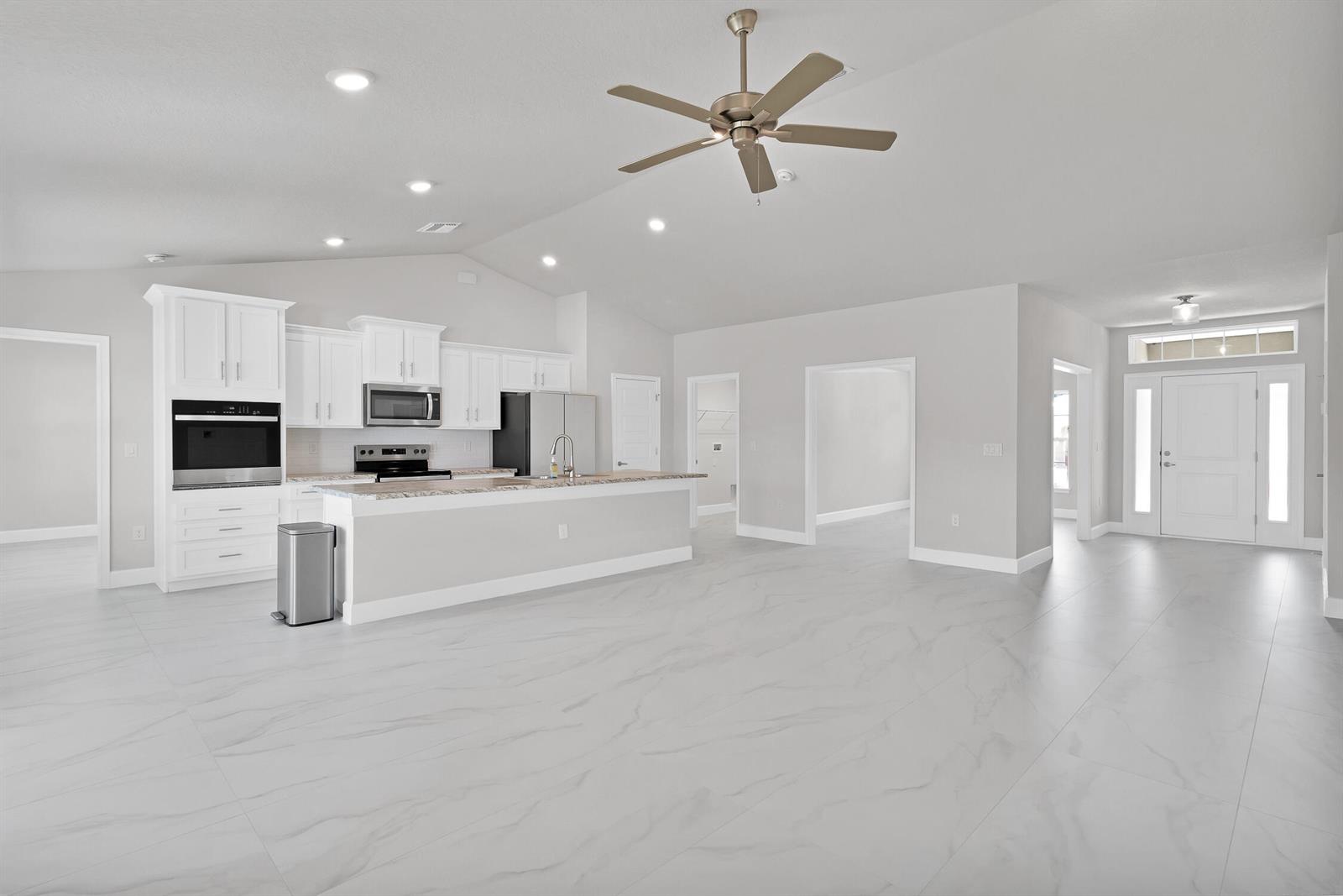 A bright, open-concept kitchen and living area features white cabinetry, stainless appliances, and marble-look flooring — 170 Spring Valley Avenue, Sebastian FL 32958, SEBASTIAN, FL