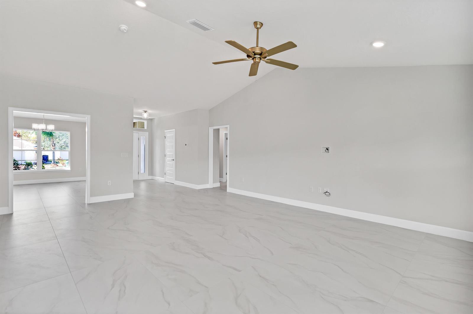 A bright, empty living room features vaulted ceilings, a gold ceiling fan, and marble-look tile — 170 Spring Valley Avenue, Sebastian FL 32958, SEBASTIAN, FL