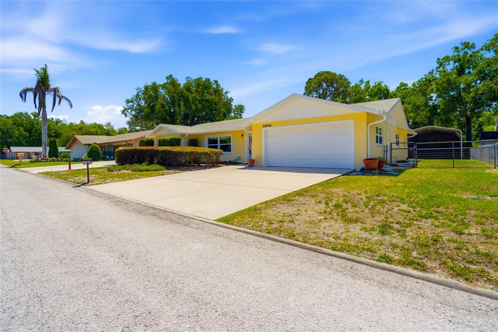 A yellow single-story house with a white garage door and a concrete driveway — 26916 MAGNOLIA BOULEVARD, LUTZ, FL