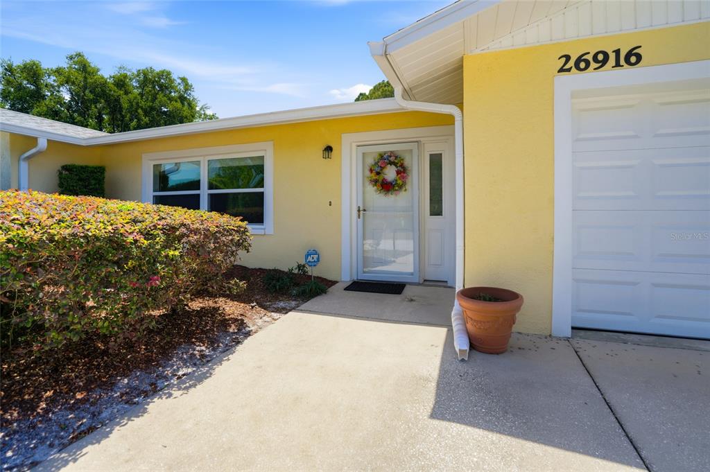 The exterior of a yellow house features a white front door, garage, and landscaping — 26916 MAGNOLIA BOULEVARD, LUTZ, FL