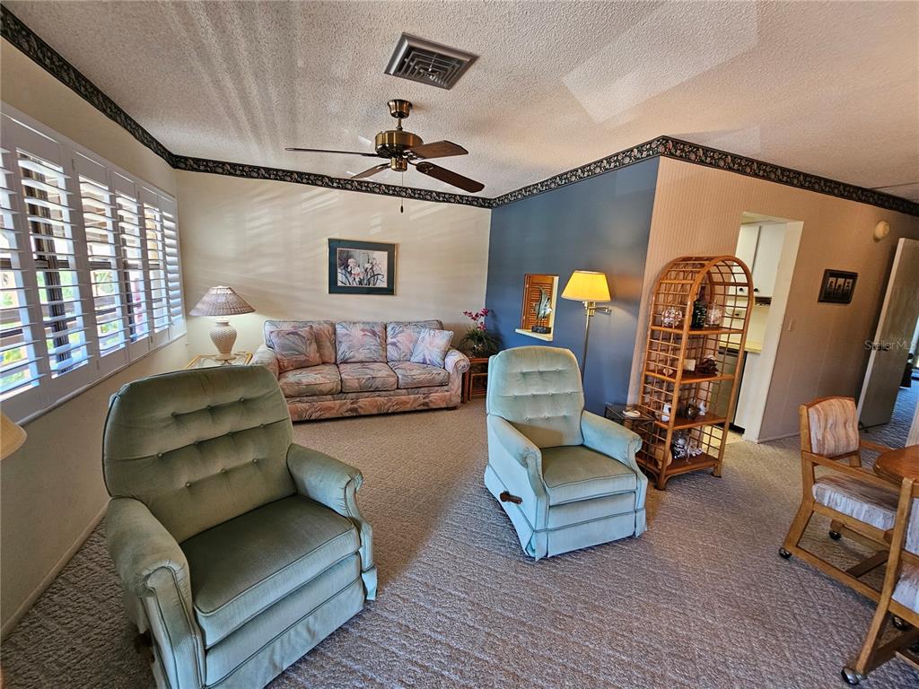 A living room features two sage green armchairs, a floral sofa, and a wicker shelf — 6 QUAILS RUN BOULEVARD UNIT 9, ENGLEWOOD, FL