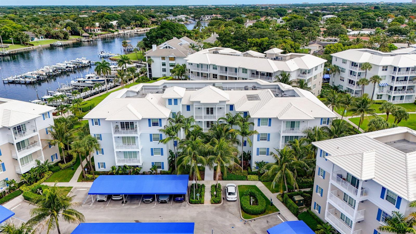 An aerial view shows a multi-story apartment complex with white buildings, blue shutters, and carports — 712 Bay Colony Drive S, Juno Beach FL 33408, JUNO BEACH, FL