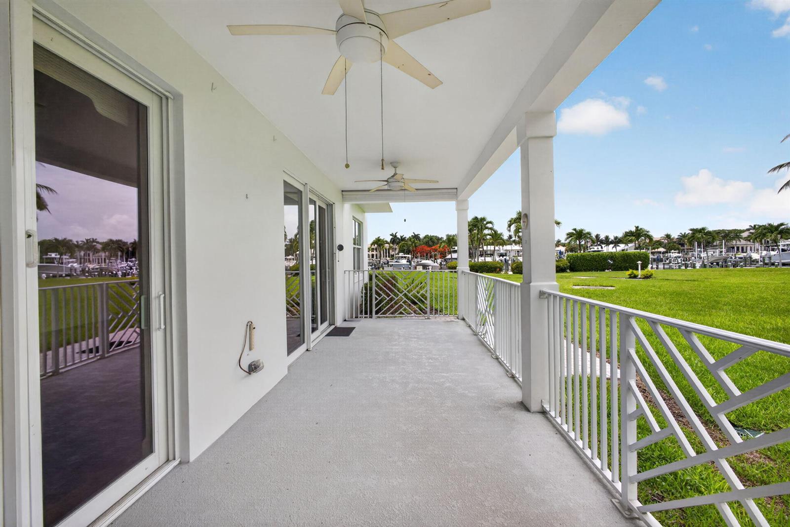 A covered patio with a white railing overlooks a grassy lawn and a boat marina — 712 Bay Colony Drive S, Juno Beach FL 33408, JUNO BEACH, FL