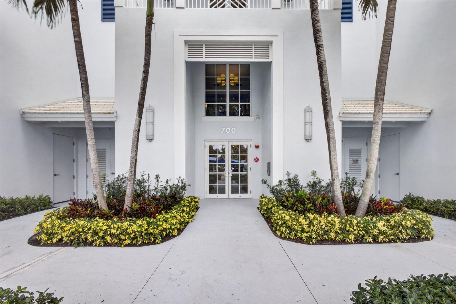 The exterior of a white building features a central entrance with the number 700 — 712 Bay Colony Drive S, Juno Beach FL 33408, JUNO BEACH, FL
