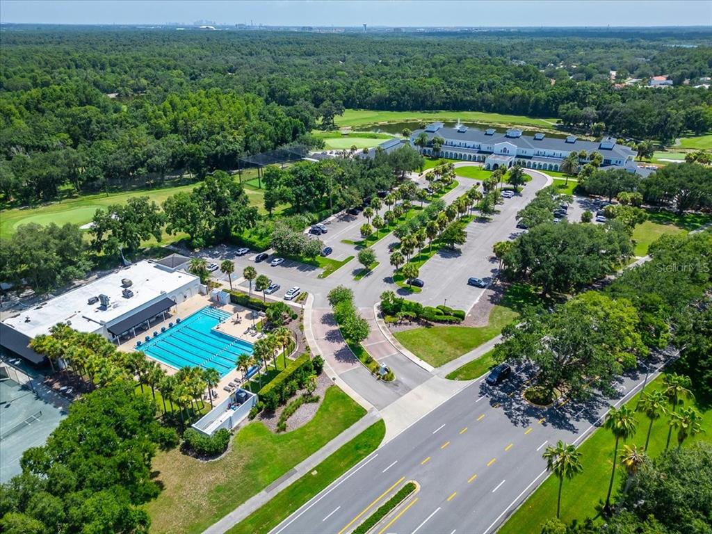 An aerial view shows a swimming pool, parking lot, and clubhouse surrounded by green trees — 15707 COCHESTER ROAD, TAMPA, FL