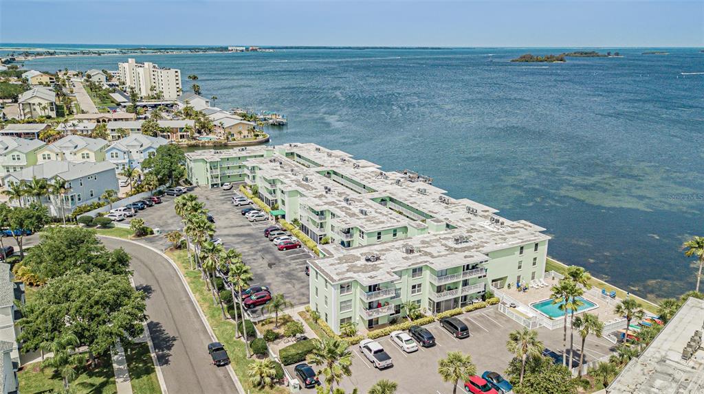 An aerial view shows a multi-story apartment complex with a parking lot and swimming pool — 464 PAULA DRIVE N UNIT 116, DUNEDIN, FL