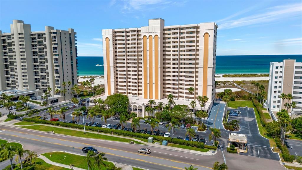 An aerial view shows three tall beachfront condominium buildings with parking lots and palm trees — 1270 GULF BOULEVARD UNIT 406, CLEARWATER, FL