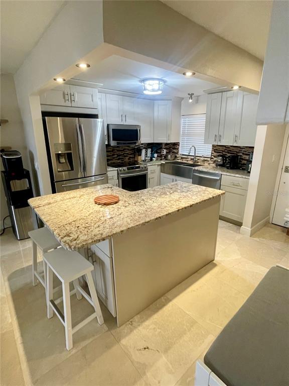 A kitchen features white cabinetry, granite countertops, stainless steel appliances, and a tile backsplash — 1270 GULF BOULEVARD UNIT 406, CLEARWATER, FL