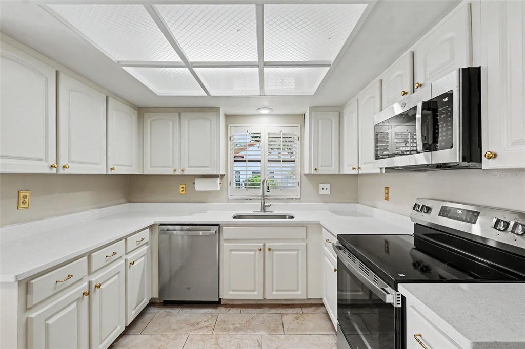 A white kitchen with stainless steel appliances, light countertops, and a grid-patterned ceiling light fixture — 11502 ROBLES DEL RIO PLACE, TEMPLE TERRACE, FL