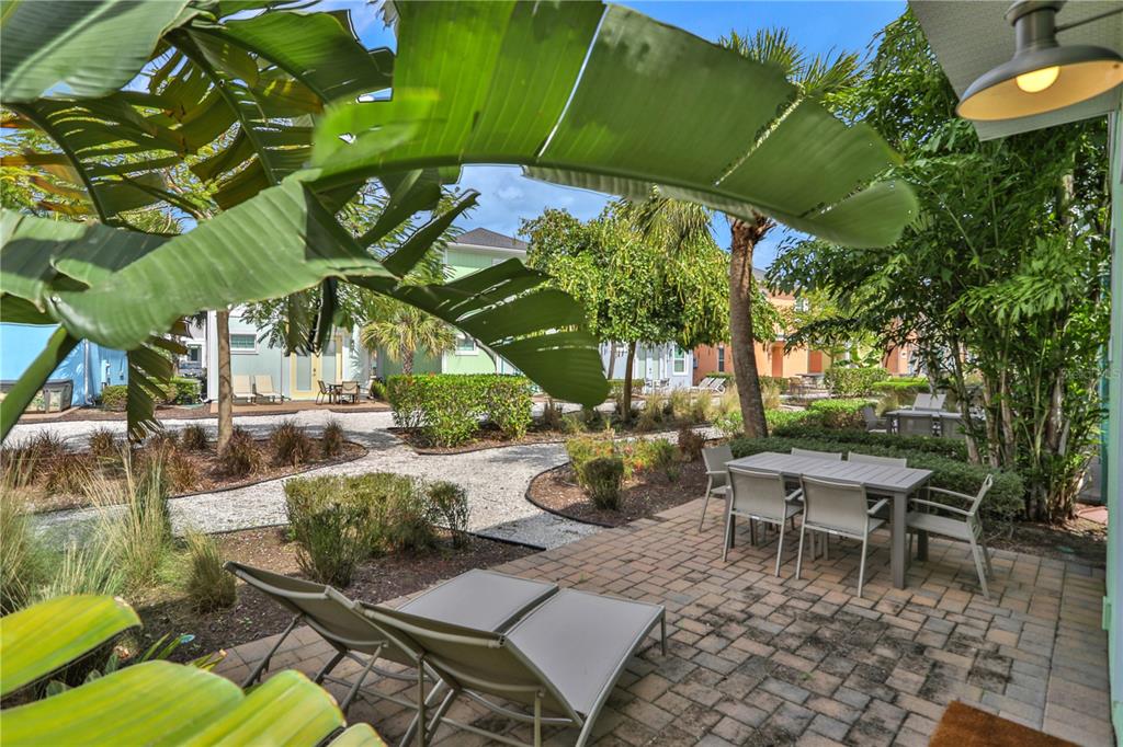 A patio with a dining set and lounge chairs overlooks a landscaped courtyard with gravel paths — 8061 LOST SHAKER LANE, KISSIMMEE, FL