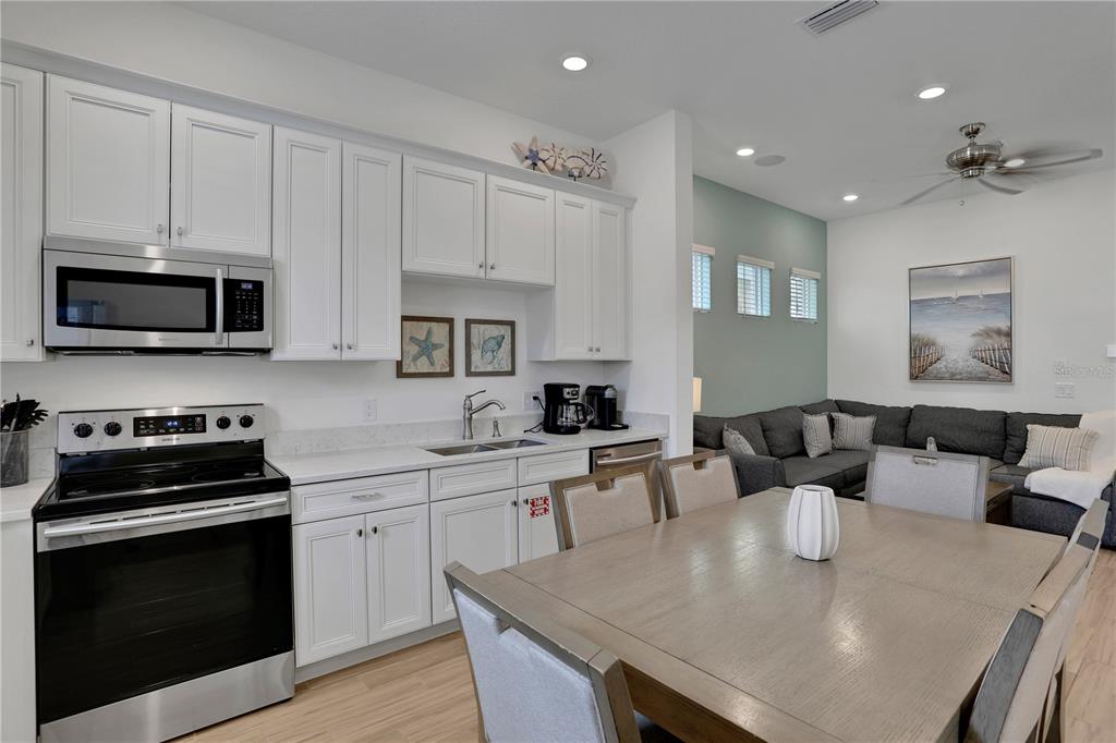 A kitchen with white cabinets and stainless steel appliances opens into a dining and living area — 8061 LOST SHAKER LANE, KISSIMMEE, FL