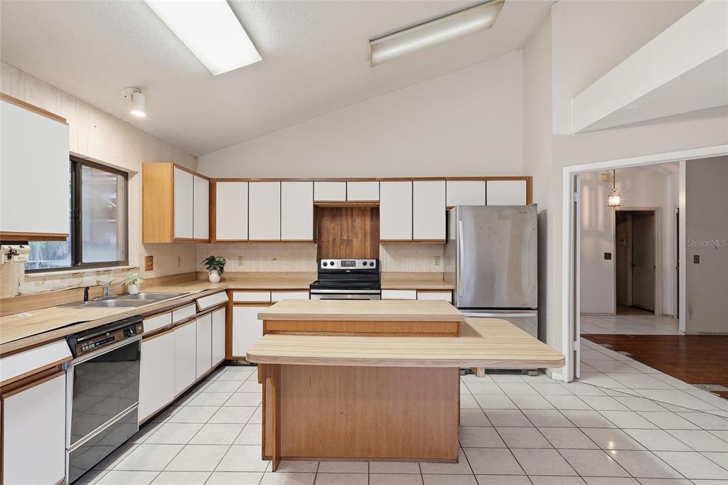 A kitchen features white cabinets, wood-trimmed laminate countertops, a central island, and white tile flooring — 2939 DANFORTH DRIVE, ORLANDO, FL