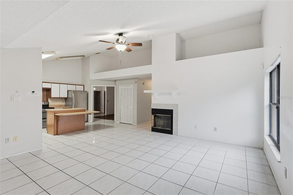 An open-concept living room and kitchen featuring white tile floors, a fireplace, and vaulted ceilings — 2939 DANFORTH DRIVE, ORLANDO, FL