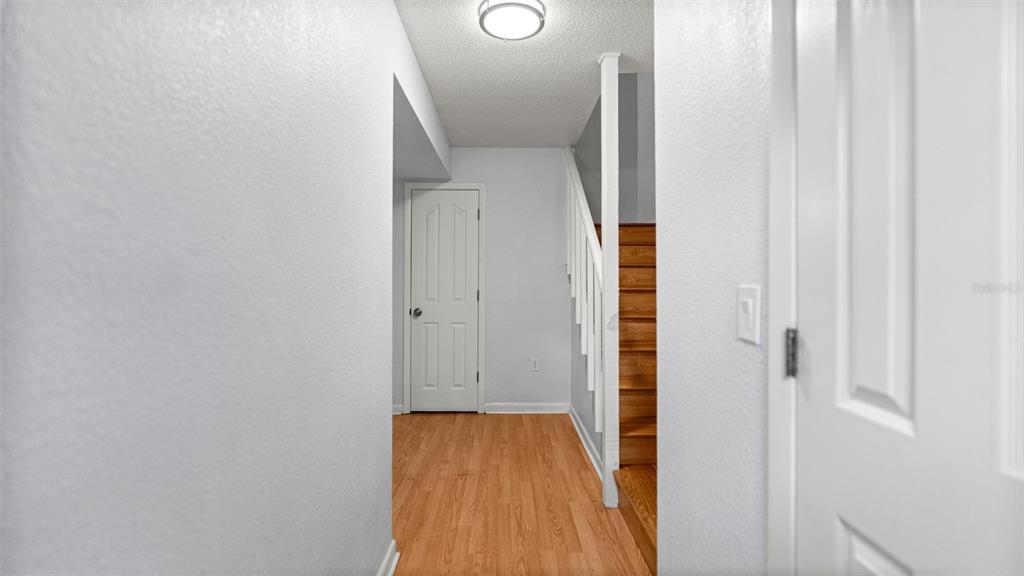 A hallway with wood-look flooring leads to a closed door and a wooden staircase — 501 SW 75TH STREET UNIT B5, GAINESVILLE, FL