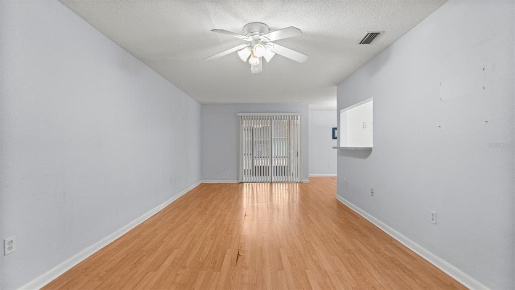 An empty living room features light-colored walls, wood-look flooring, a ceiling fan, and sliding glass doors — 501 SW 75TH STREET UNIT B5, GAINESVILLE, FL
