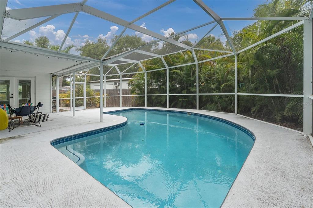 A screened-in patio features a swimming pool with blue tile trim and surrounding concrete decking — 4986 WOODLAND DRIVE, ST PETERSBURG, FL