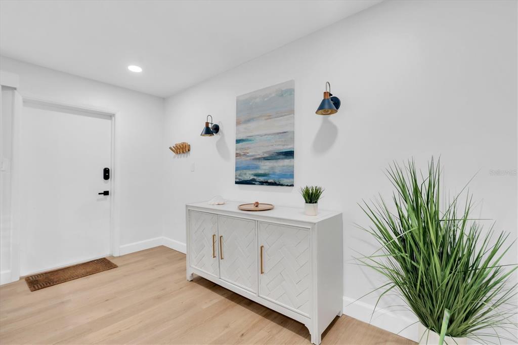 A white entryway features a wooden floor, a white cabinet, wall sconces, and artwork — 4986 WOODLAND DRIVE, ST PETERSBURG, FL