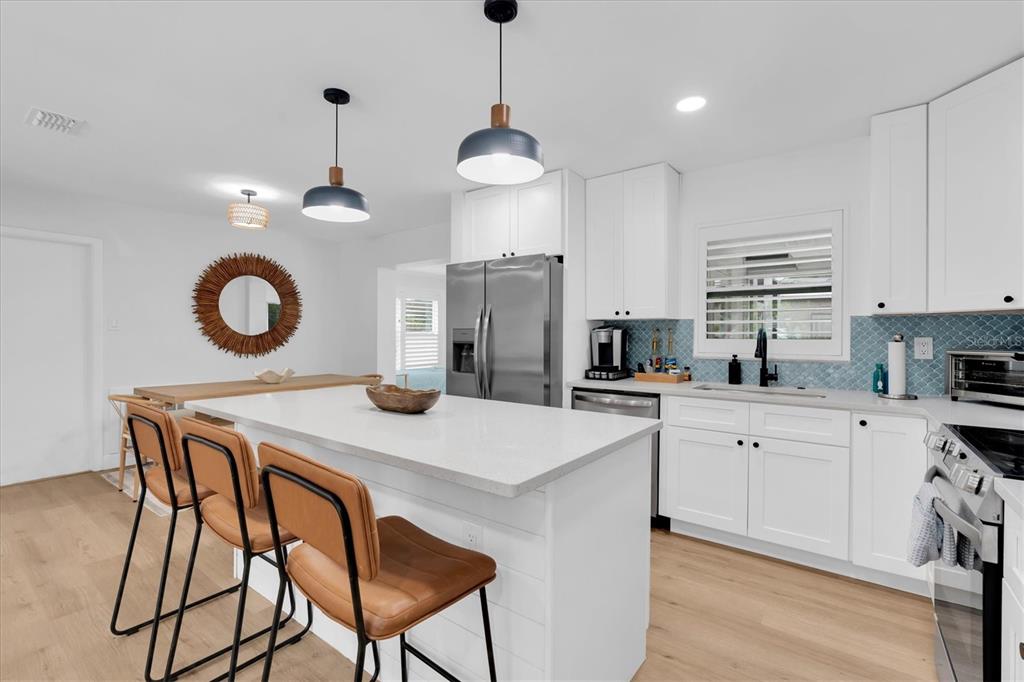A modern kitchen features a white island with bar stools, stainless appliances, and blue backsplash — 4986 WOODLAND DRIVE, ST PETERSBURG, FL