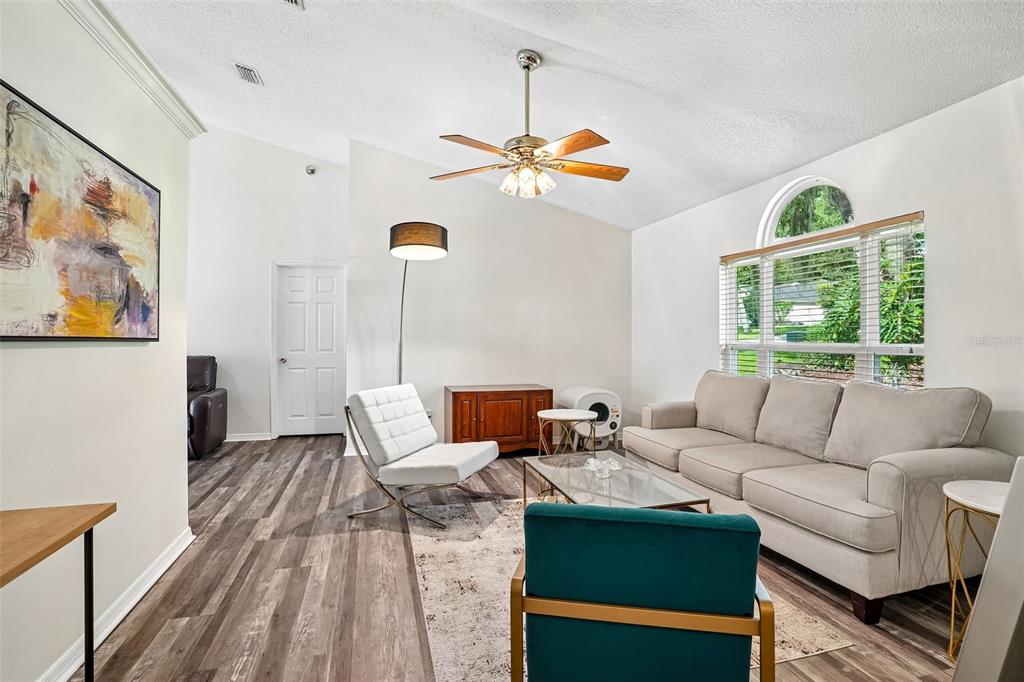 A living room features a vaulted ceiling, wood-look flooring, a beige sofa, and a ceiling fan — 1167 WOODLAND TERRACE TRAIL, ALTAMONTE SPRINGS, FL