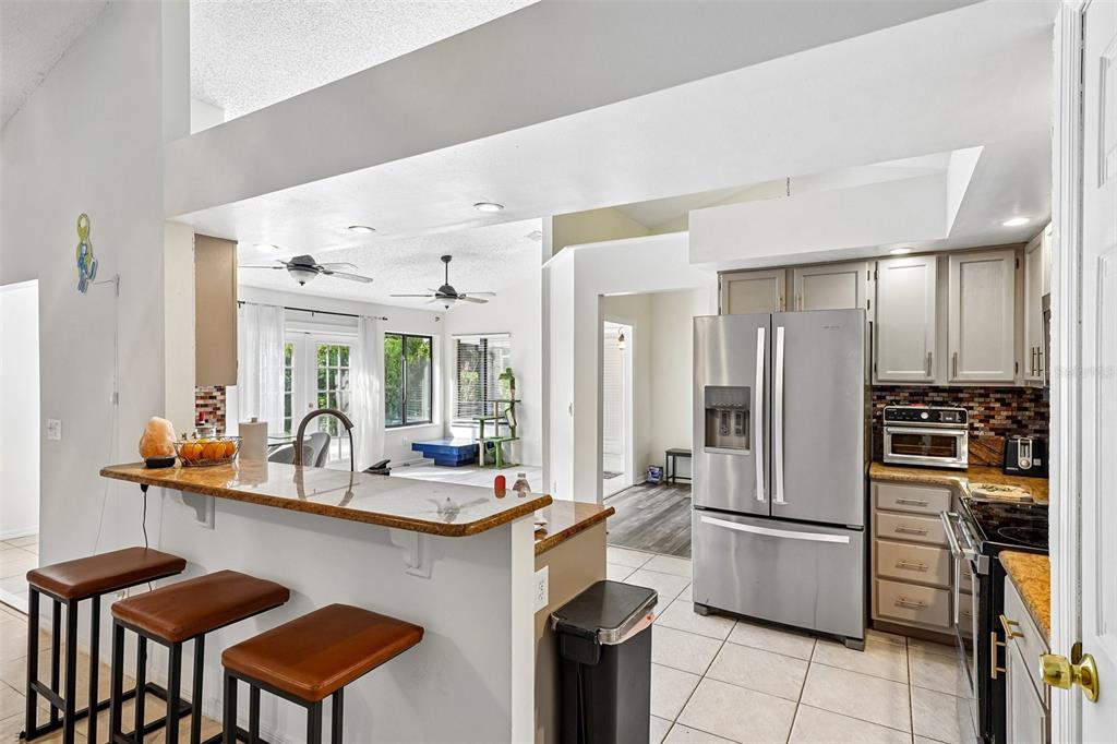 A kitchen with a breakfast bar, stainless steel appliances, and tile flooring overlooks a living area — 1167 WOODLAND TERRACE TRAIL, ALTAMONTE SPRINGS, FL