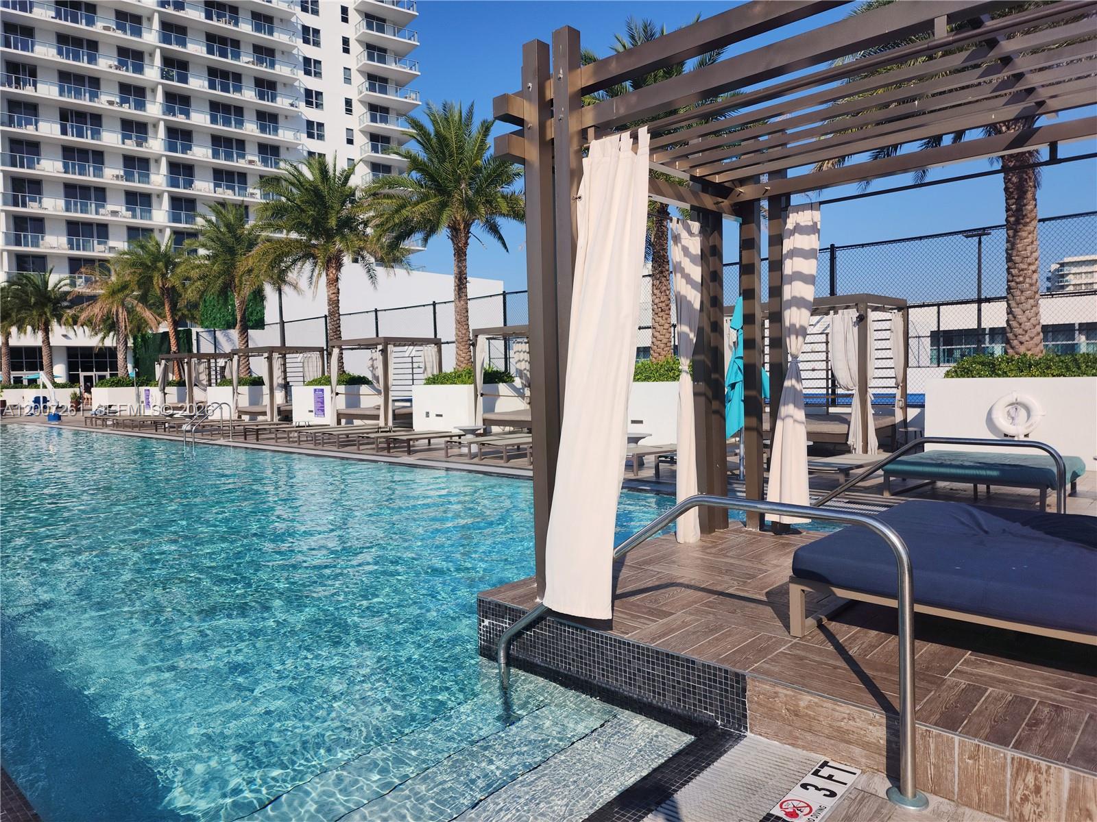 A swimming pool with lounge chairs and cabanas under a pergola on a sunny day — 4010 S Ocean Dr # R2905, Hollywood FL 33019, HOLLYWOOD, FL