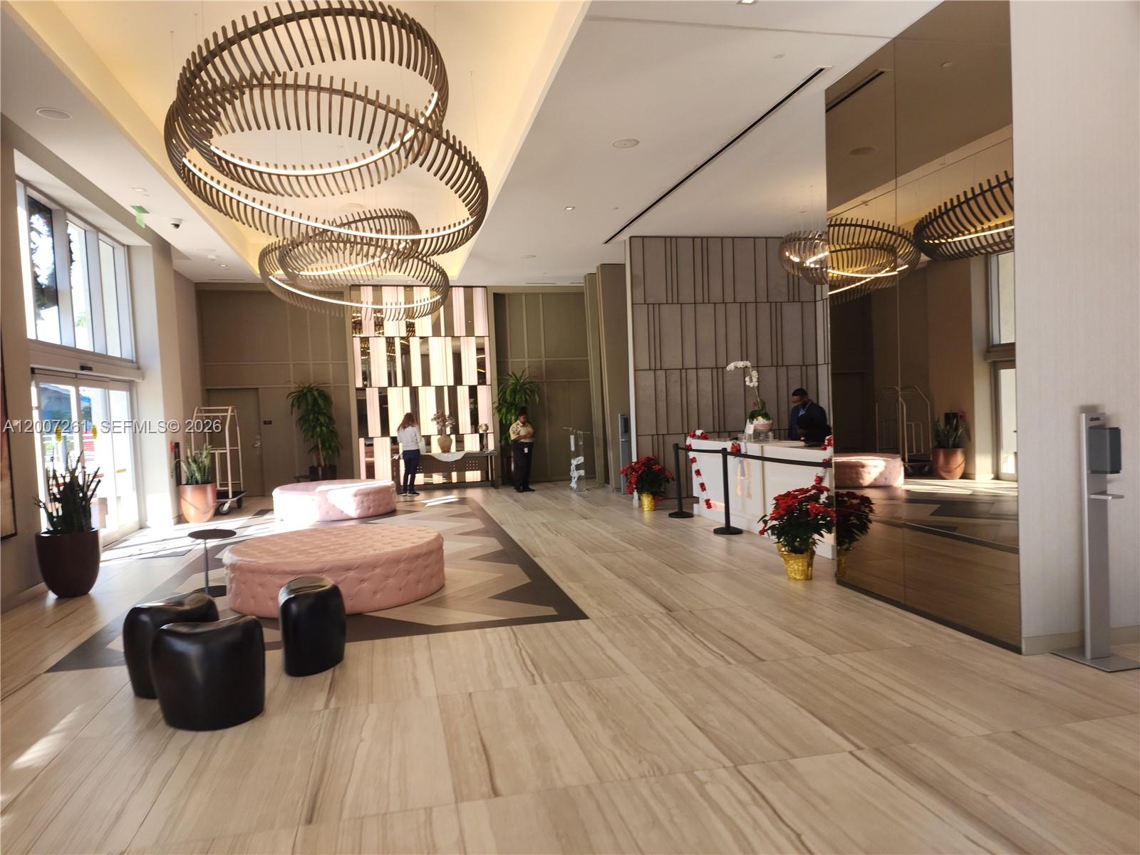 A modern hotel lobby features circular light fixtures, pink tufted ottomans, and a reception desk — 4010 S Ocean Dr # R2905, Hollywood FL 33019, HOLLYWOOD, FL