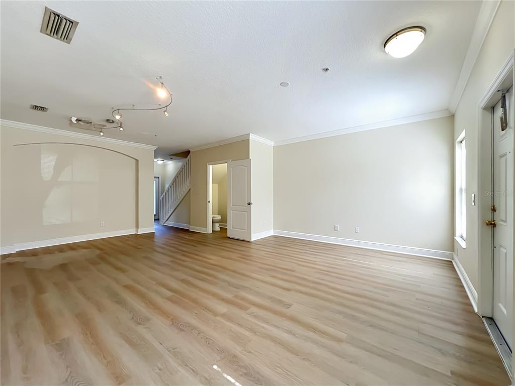 An empty living room features light wood-look flooring, beige walls, a staircase, and recessed lighting — 13232 DANIELS LANDING CIRCLE, WINTER GARDEN, FL