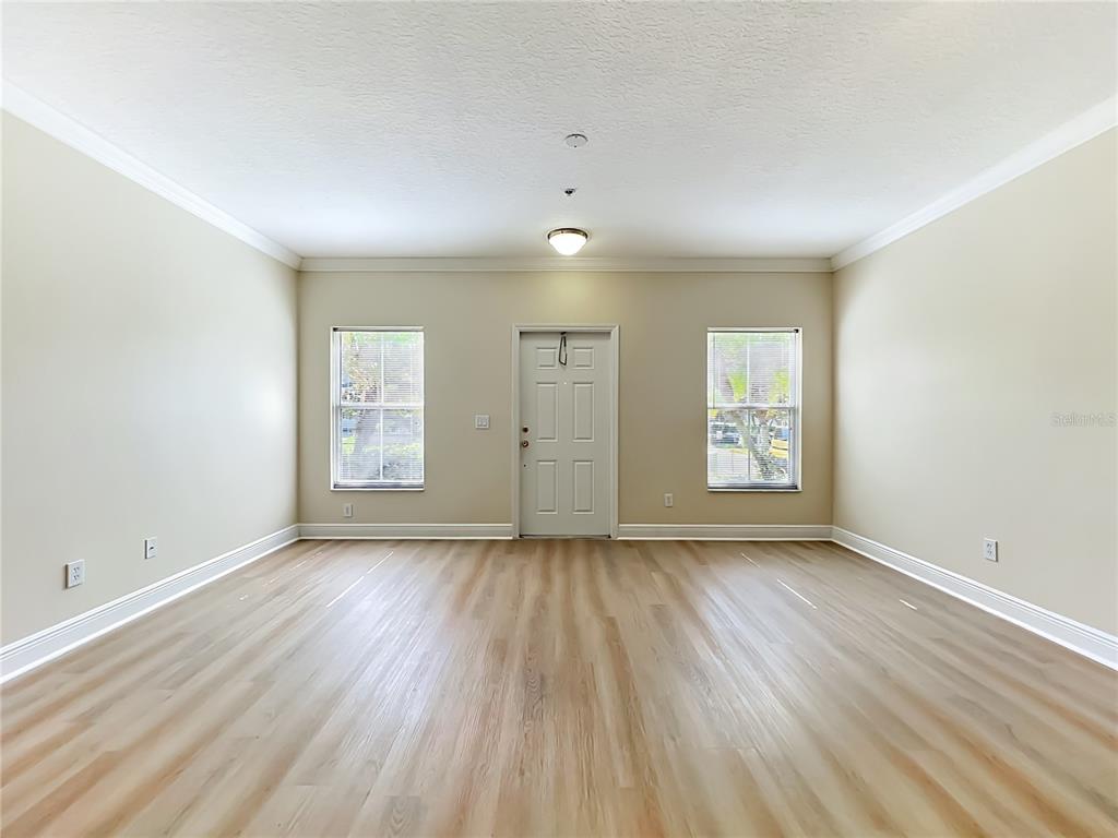 An empty room features light-colored wood-look flooring, beige walls, two windows, and a central door — 13232 DANIELS LANDING CIRCLE, WINTER GARDEN, FL