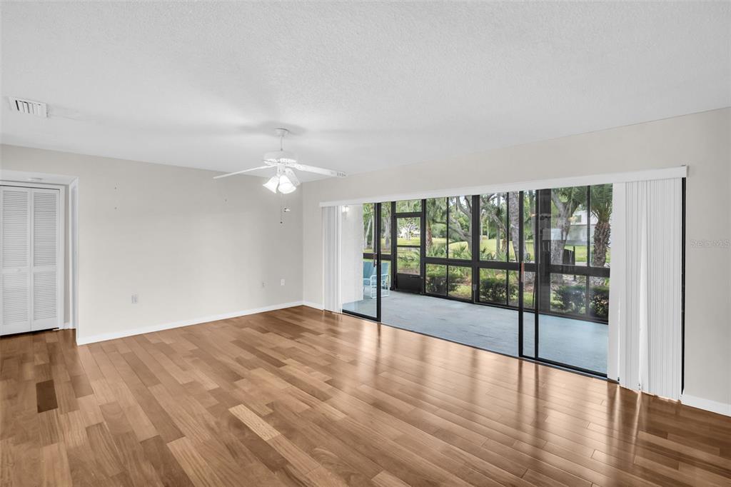 A living room with hardwood floors, a ceiling fan, and large sliding glass doors to a lanai — 120 EVELYN COURT, OLDSMAR, FL