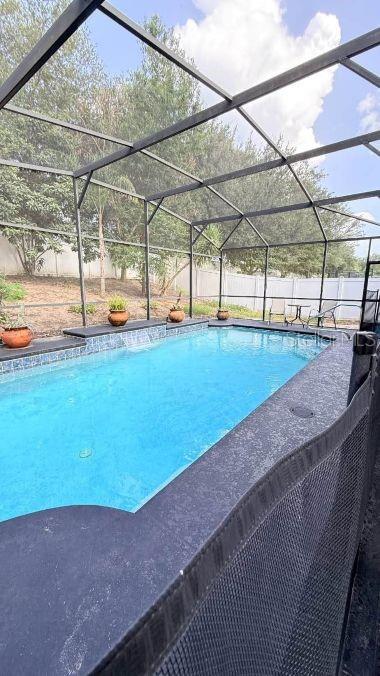 A rectangular swimming pool with a screen enclosure and a safety fence in the foreground — 218 TRES REYES LANE, GROVELAND, FL