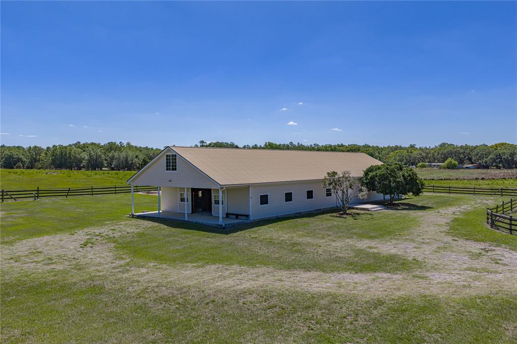 An exterior view of a long, light-colored barn with a metal roof in a field — 29001 BAYHEAD ROAD, DADE CITY, FL