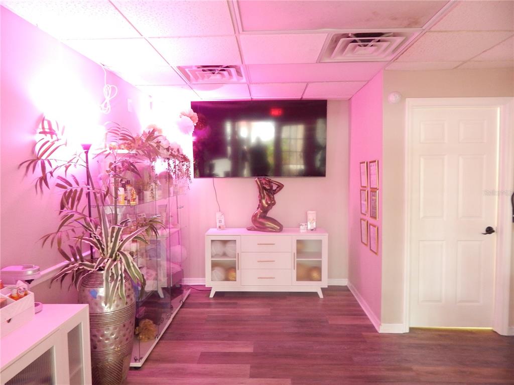 A room with pink lighting, a wall-mounted television, a white cabinet, and a glass display case — 705 E OAK STREET UNIT B, KISSIMMEE, FL