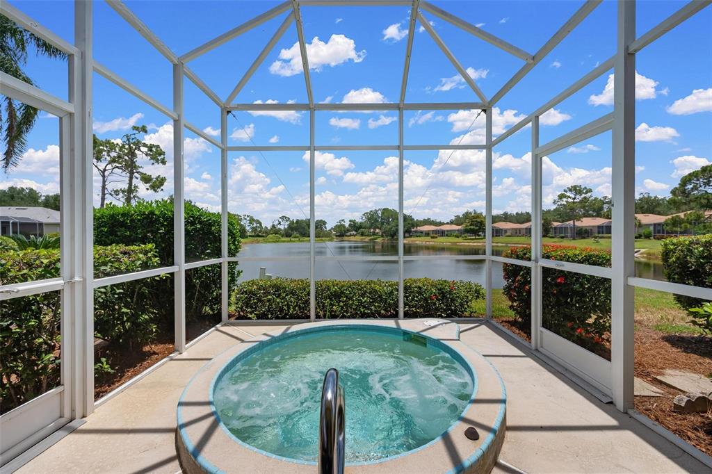 A round hot tub sits inside a screened-in lanai overlooking a lake and neighborhood homes — 880 CHALMERS DRIVE UNIT 880, VENICE, FL