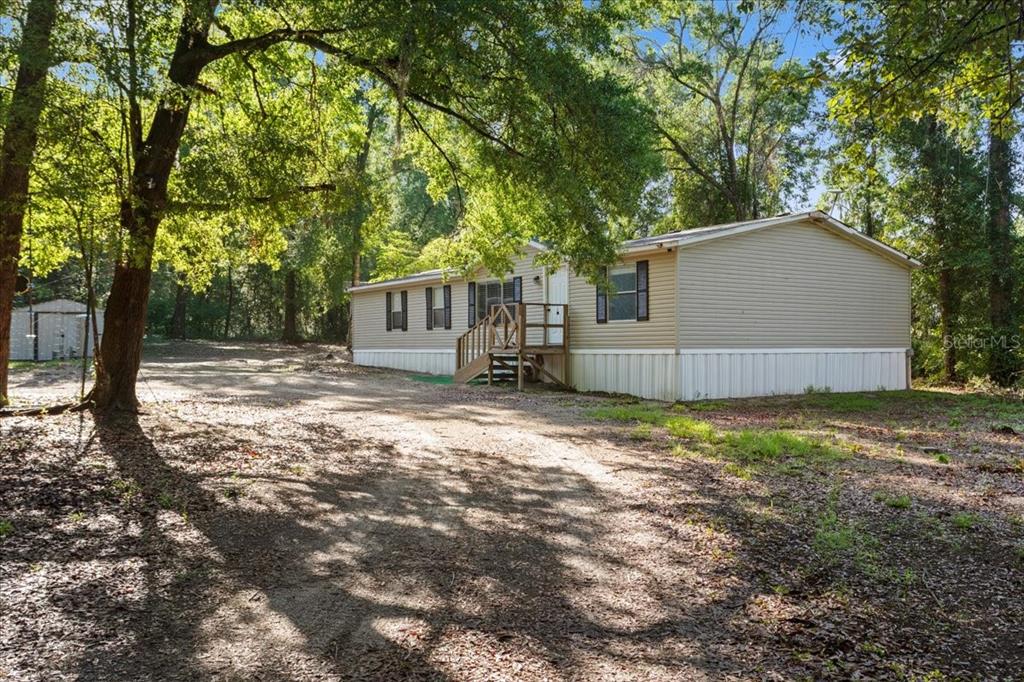 A tan mobile home with white skirting sits on a dirt lot surrounded by trees — 173 SW BOUNDARY WAY, FORT WHITE, FL