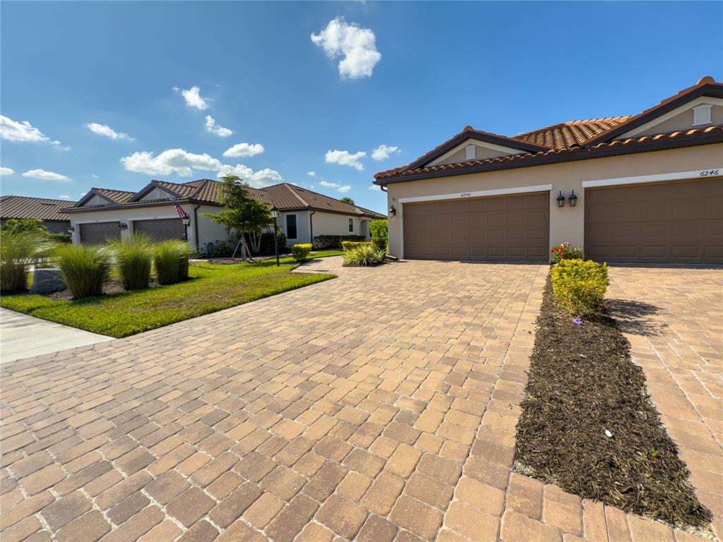 A paved driveway leads to the garages of two suburban homes under a blue sky — 6250 PLATEAU COURT, BRADENTON, FL