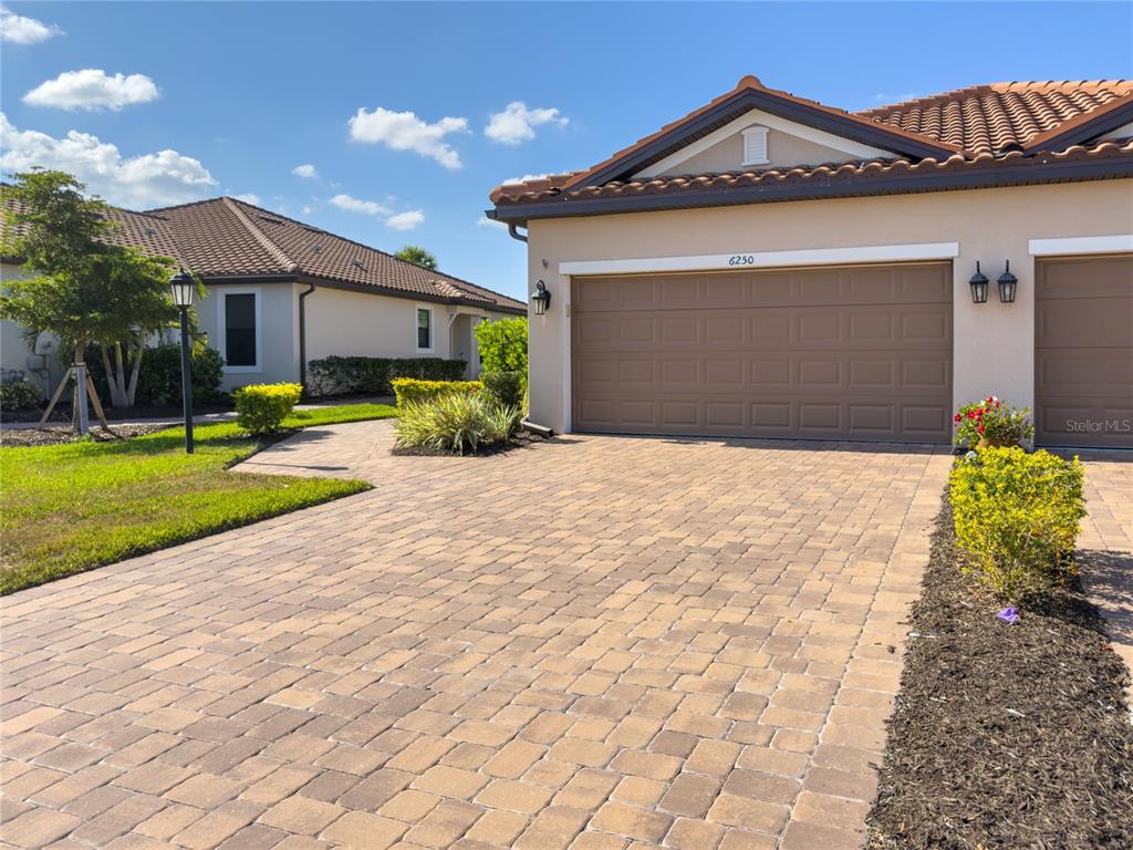 A paved driveway leads to the garage of a single-story house with a tiled roof — 6250 PLATEAU COURT, BRADENTON, FL
