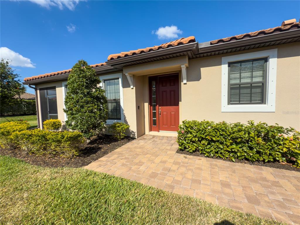 A tan stucco house exterior features a red front door, tiled roof, and landscaped yard — 6250 PLATEAU COURT, BRADENTON, FL