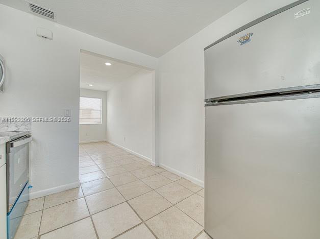 A kitchen with a stainless steel refrigerator and tiled floors leads into an adjacent room — 1887 NW 48th St # 1887, Miami FL 33142, MIAMI, FL