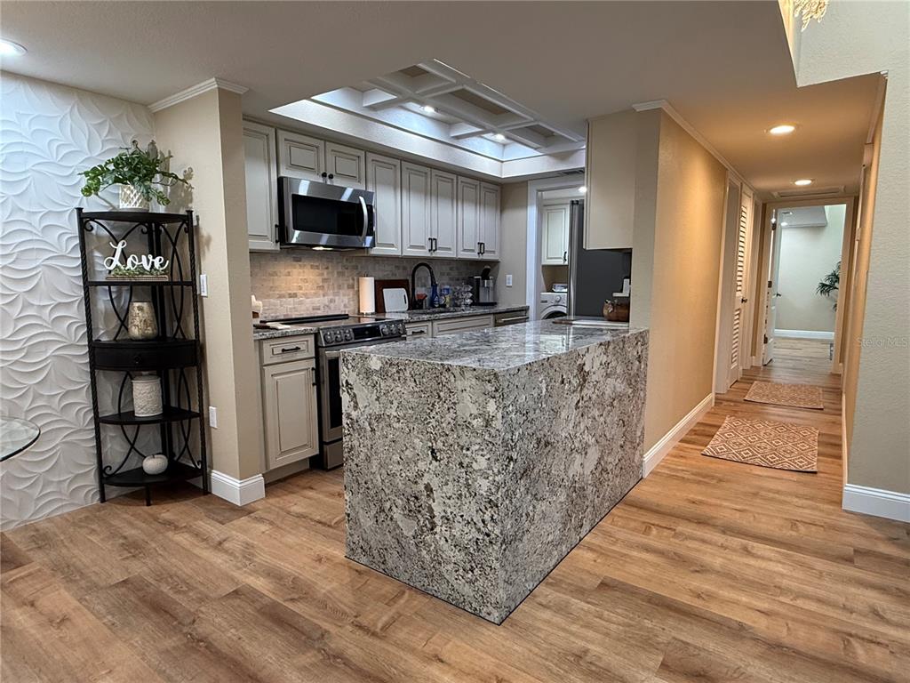 A kitchen features a granite waterfall island, light-colored cabinetry, and wood-look flooring — 6861 WOODWIND DR UNIT 75, SARASOTA, FL